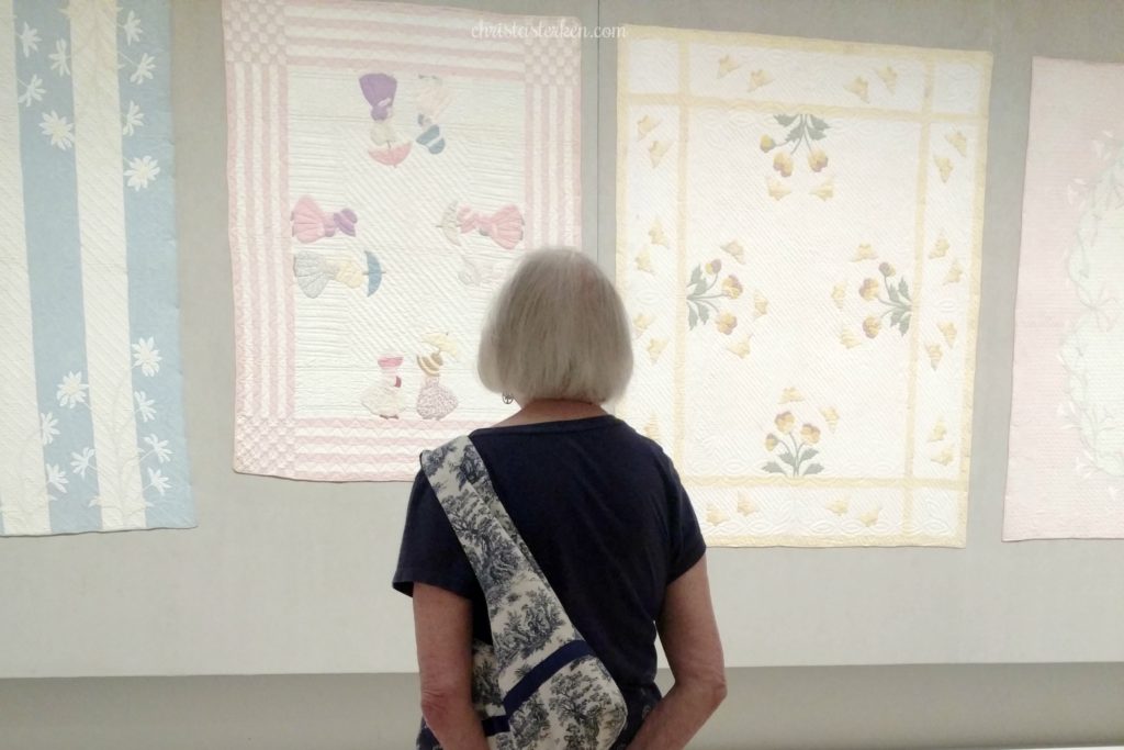 old lady looking at quilts in museum