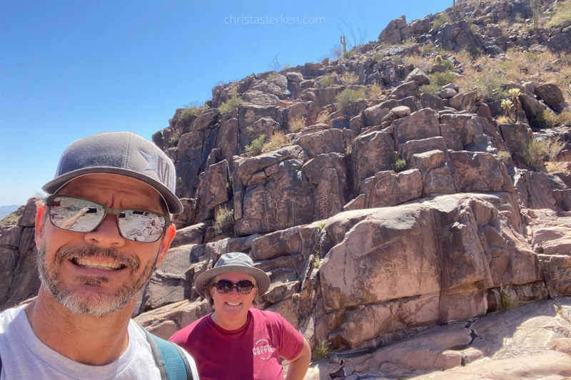 man and woman hiking by petroglyphs on desert trail
